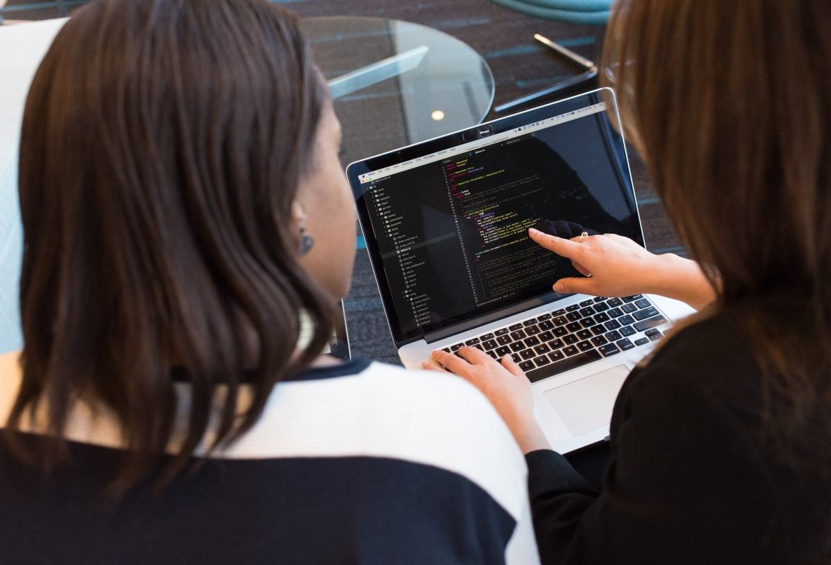 Two people looking at code on a laptop screen.