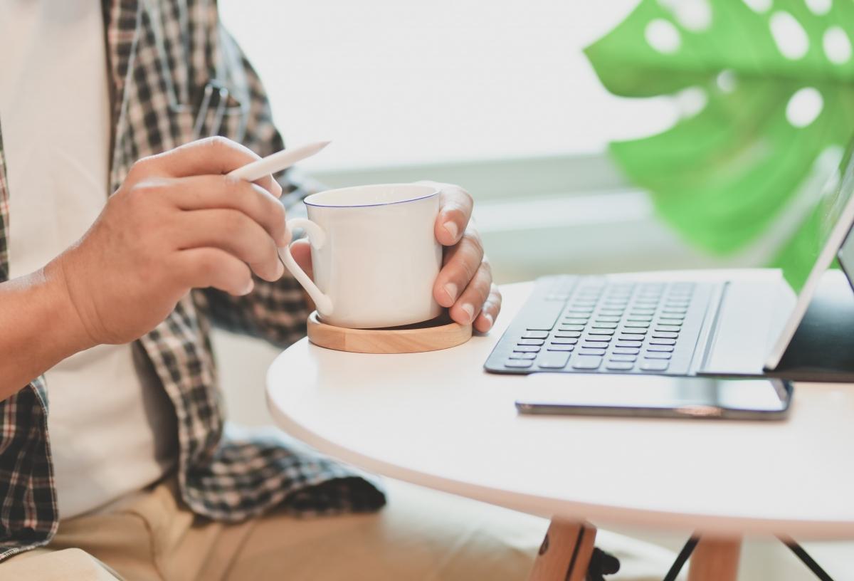 Person holding a coffee cup while working on a laptop at a round table.