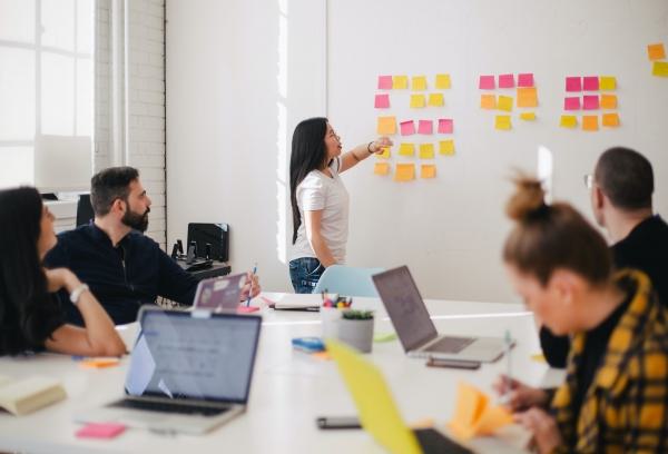 Team collaborating in a workshop with a woman placing sticky notes on a wall.